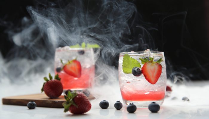 Strawberry juice cocktail with ice and mint on black background and smoke